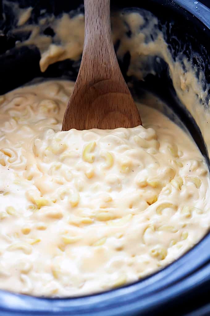 close up of slow cooker 4 cheese macaroni and a wooden spoon in a slow cooker.