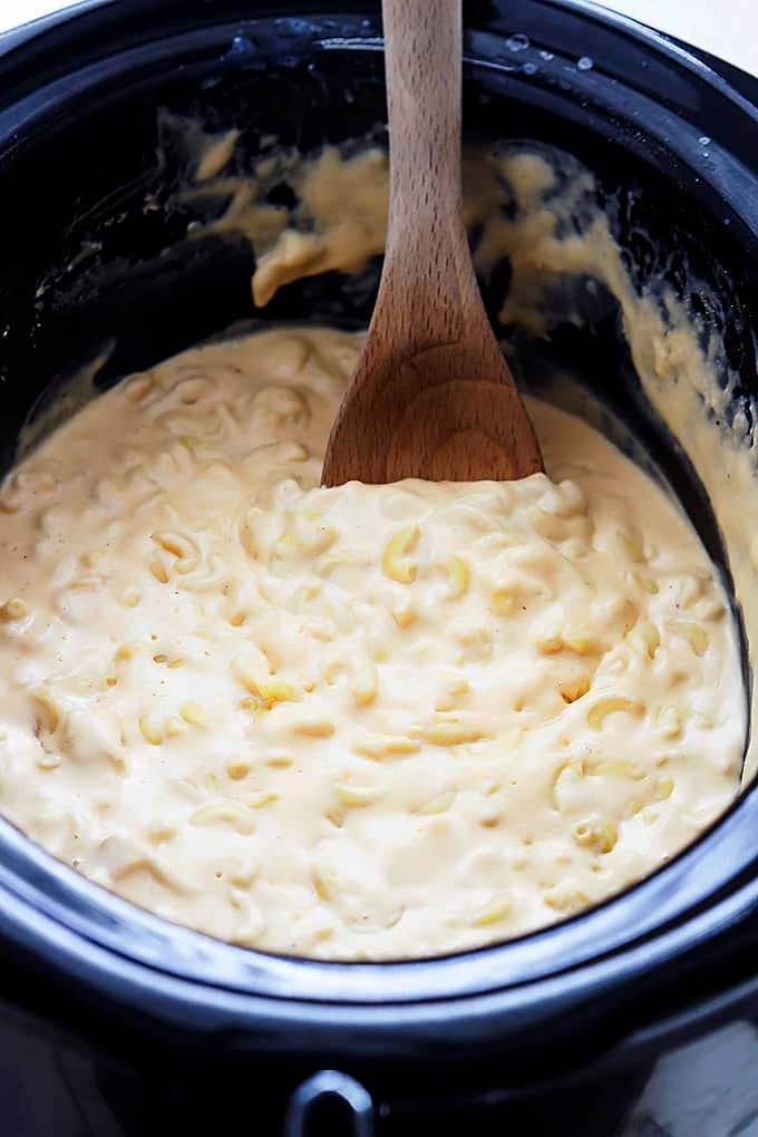 slow cooker 4 cheese macaroni with a wooden serving spoon in a slow cooker.