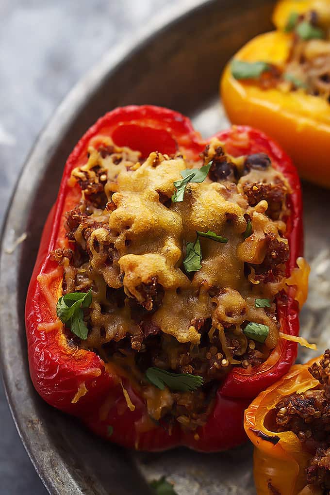 close up of a slow cooker southwest quinoa stuffed pepper with more peppers on the side all on a round serving tray.