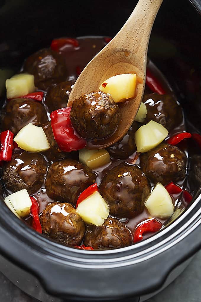 slow cooker sweet & sour meatballs with a wooden spoon in a slow cooker.
