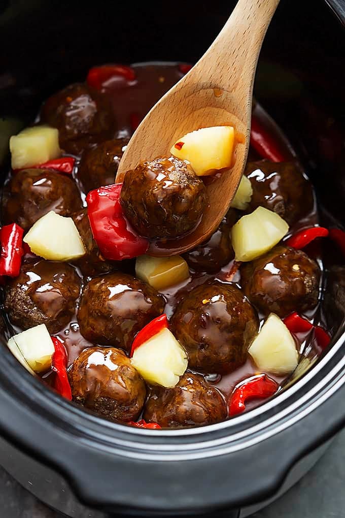 slow cooker sweet & sour meatballs with a wooden spoon in a slow cooker.