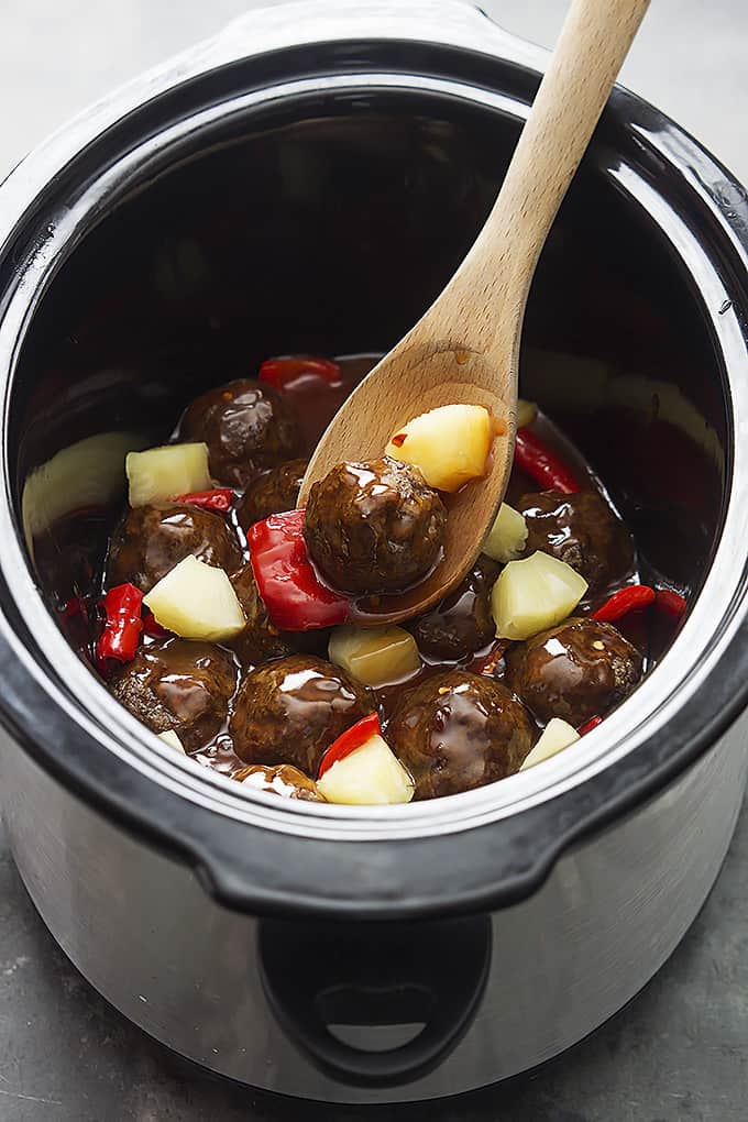 slow cooker sweet & sour meatballs with a wooden spoon in a slow cooker.