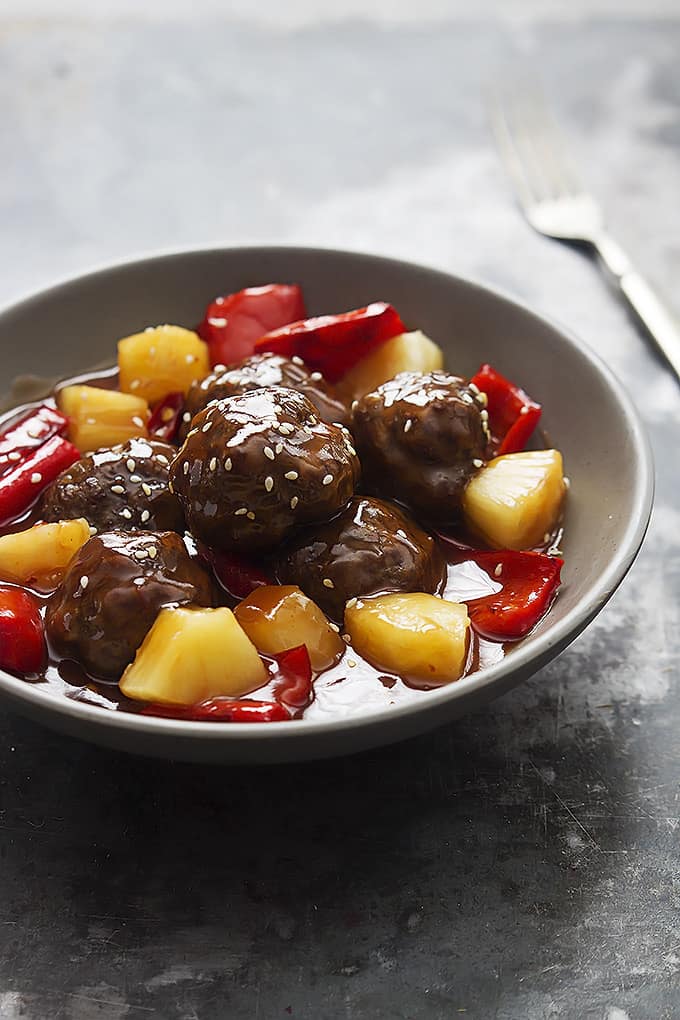 slow cooker sweet & sour meatballs in a bowl with a fork on the side.