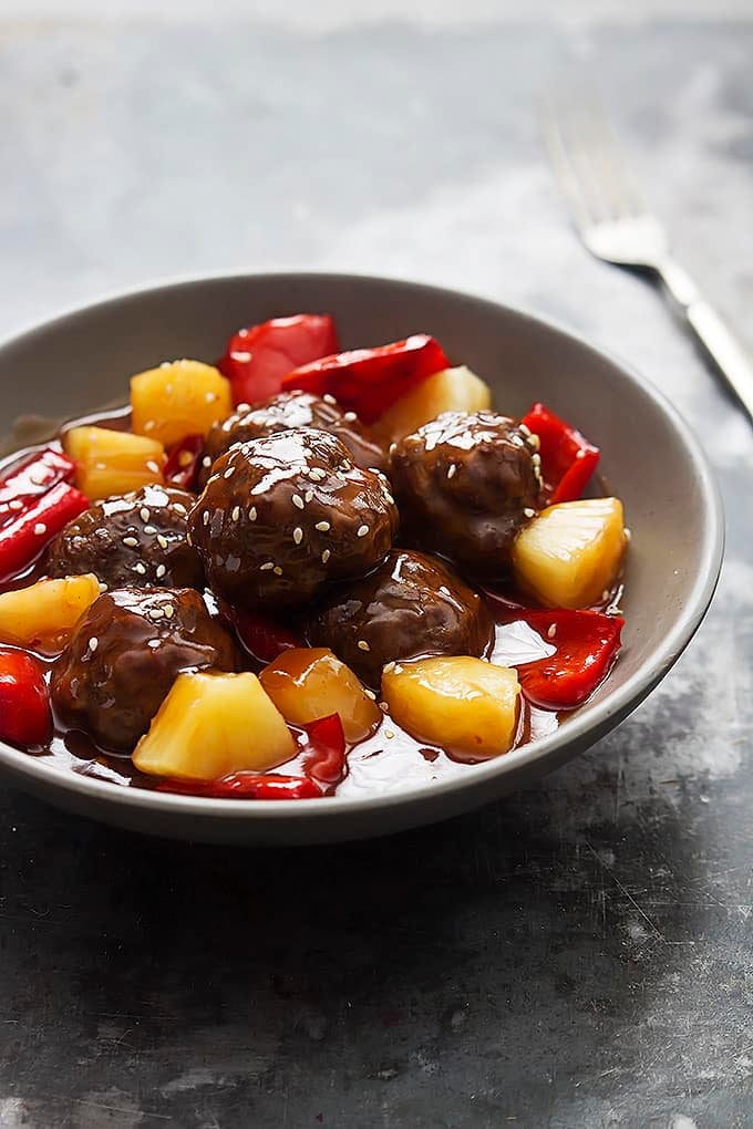 slow cooker sweet & sour meatballs in a bowl with a fork on the side.