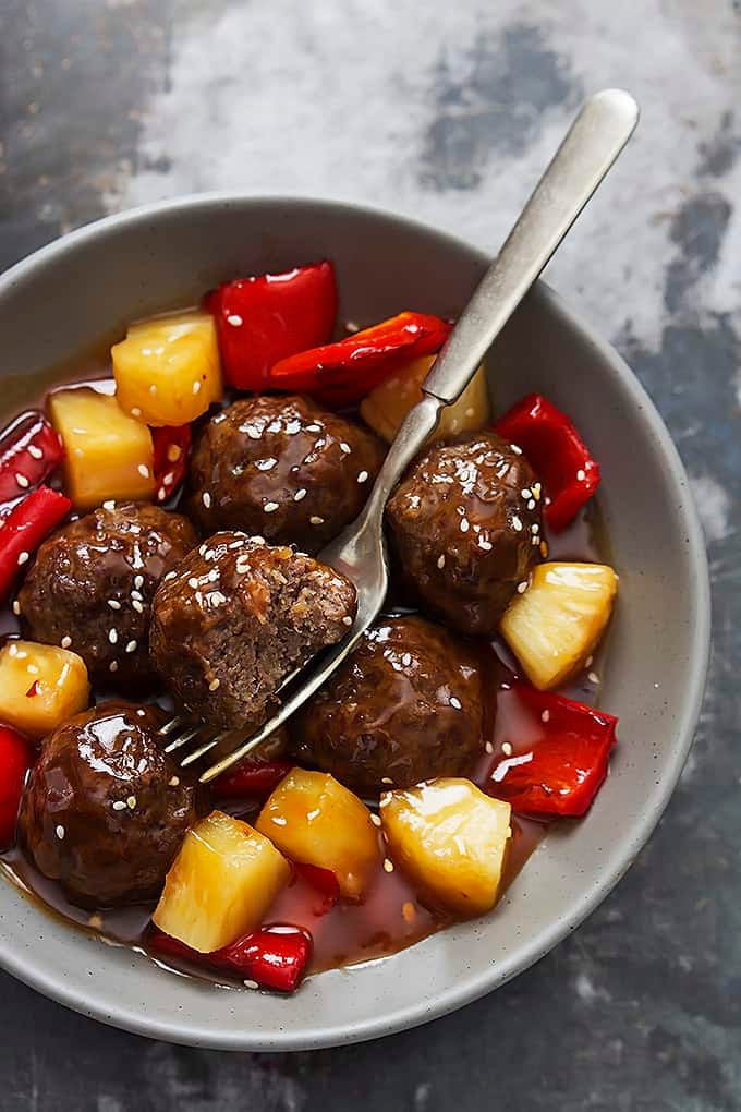 top view of slow cooker sweet & sour meatballs with a fork in a bowl.