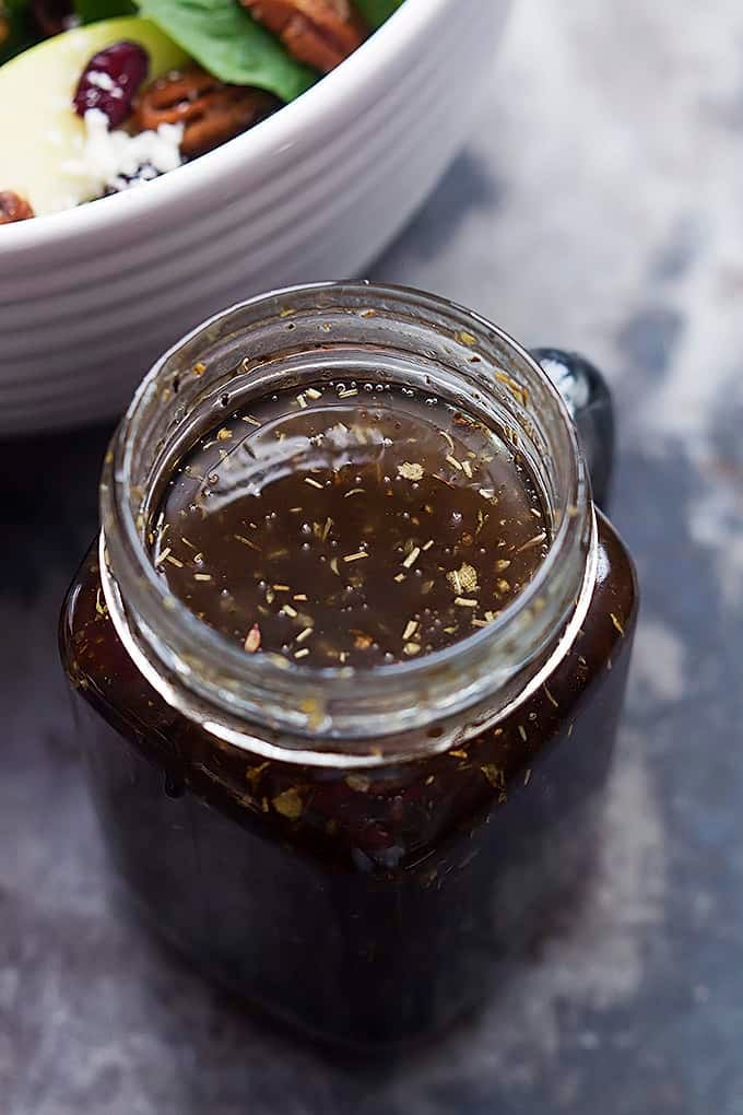 sweet balsamic dressing in a jar by a bowl of apple cherry candied pecan salad.