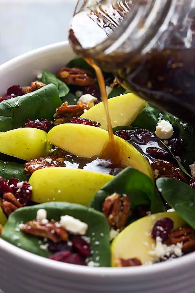 close up of apple cherry candied pecan salad in a bowl with sweet balsamic dressing being poured on top.