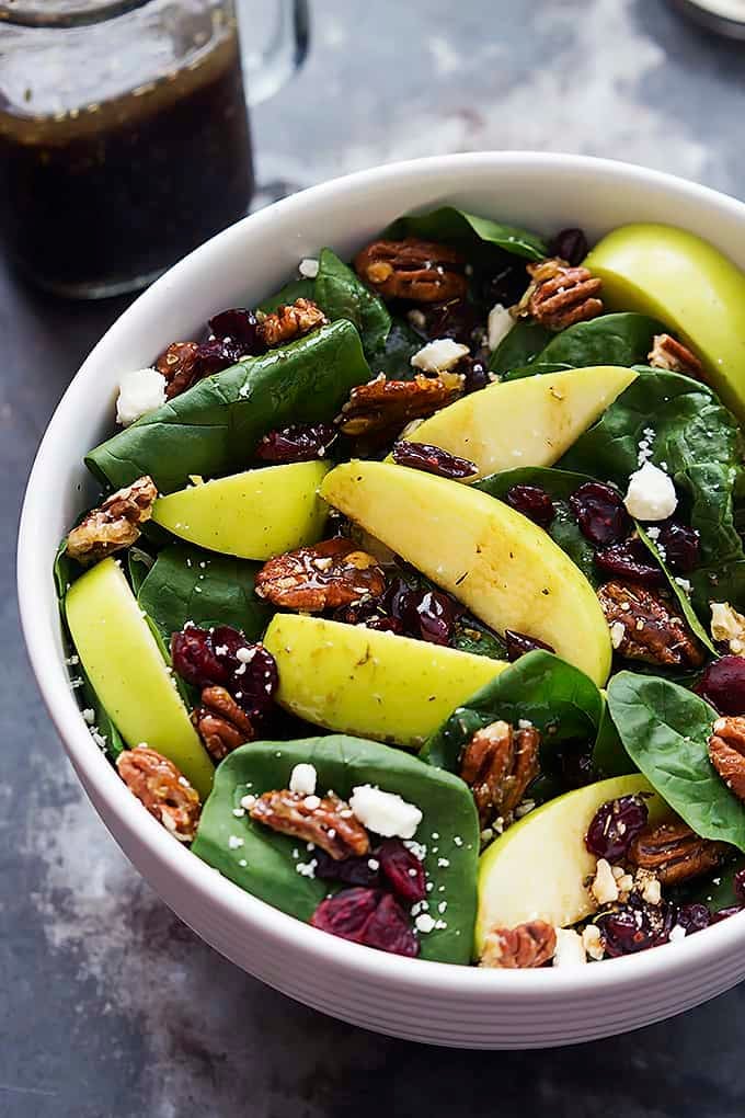 a bowl of apple cherry candied pecan salad with sweet balsamic dressing in a jar on the side.