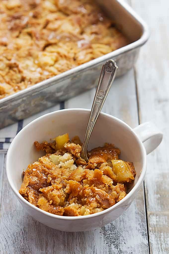 caramel apple dump cake and a fork in a bowl with more cake in a baking pan in the background.