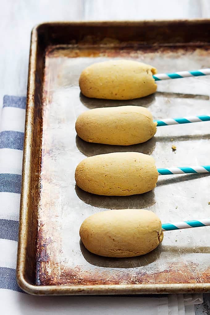 homemade baked corn dogs on sticks on a baking sheet.