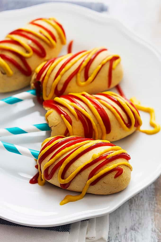 homemade baked corn dogs on sticks on a plate topped with mustard and ketchup.