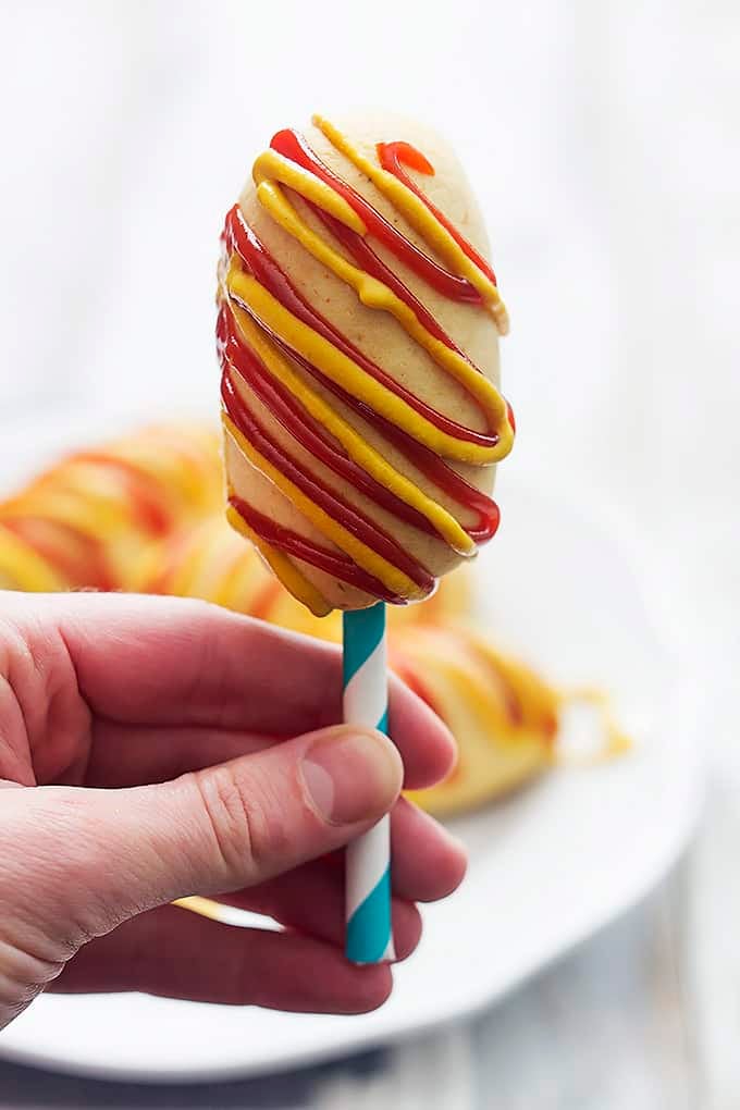 a hand holding up a homemade baked corn dogs on a stick with mustard and ketchup on it.