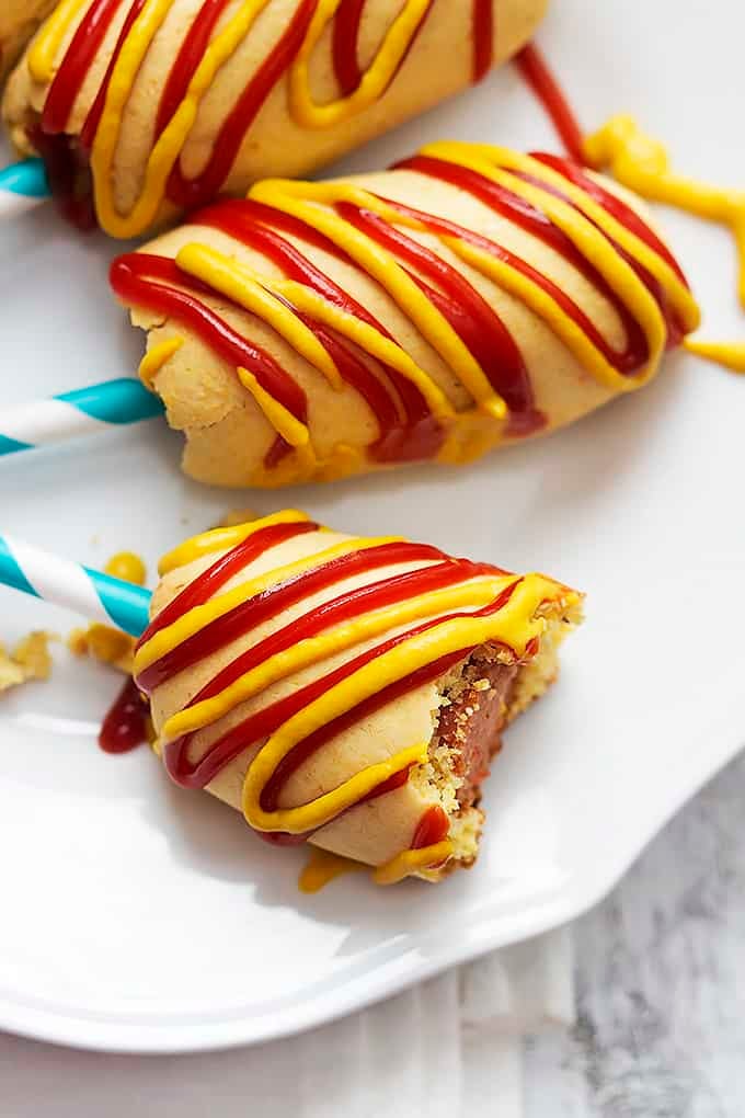 close up of a homemade baked corn dogs on sticks with mustard and ketchup on it with the front one missing a bite.