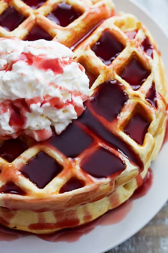 top view of Greek yogurt waffles topped with whipped cream and strawberry syrup on a plate.