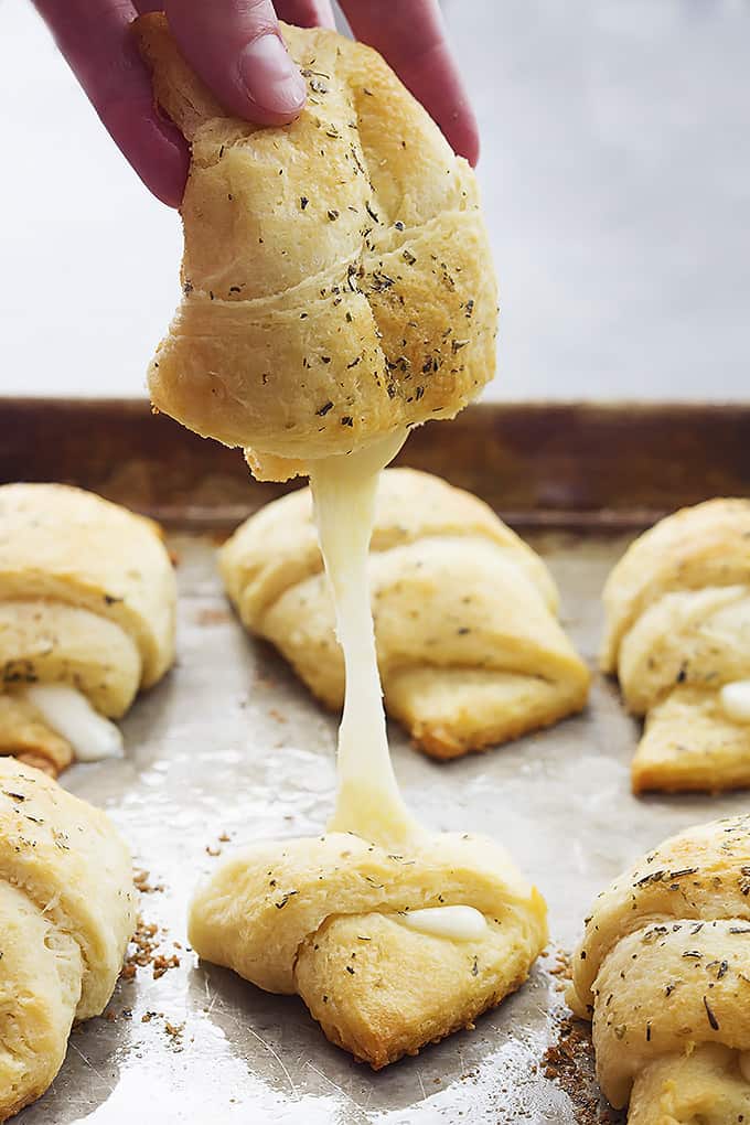 a hand picking up half of a cheesy garlic butter crescent with the other half on a baking sheet with more crescents.