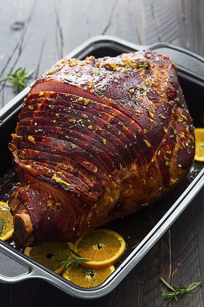 rosemary citrus ham with orange slices in a serving pan.