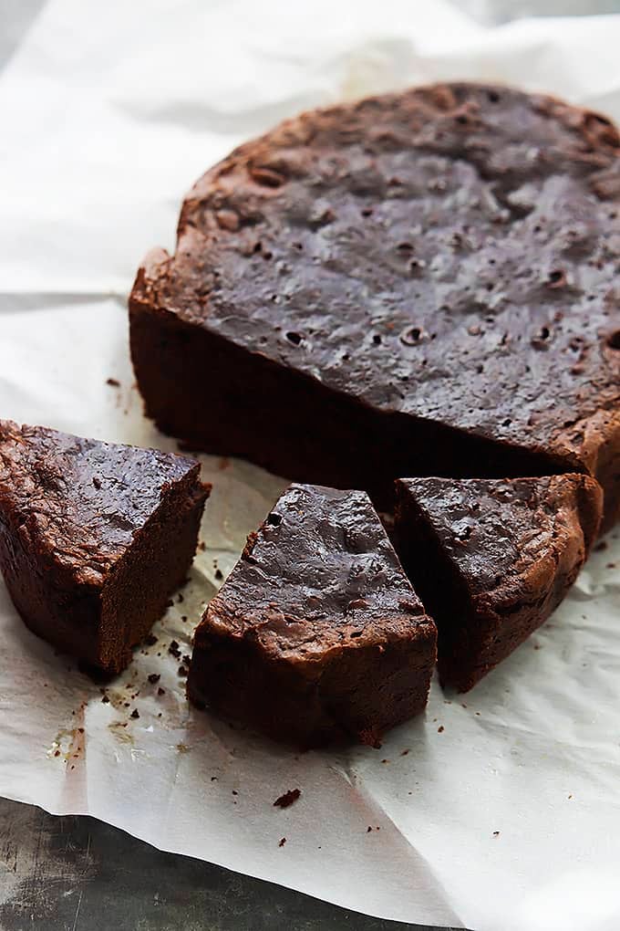 slow cooker brownies on parchment paper next to the large brownie not cut up yet.