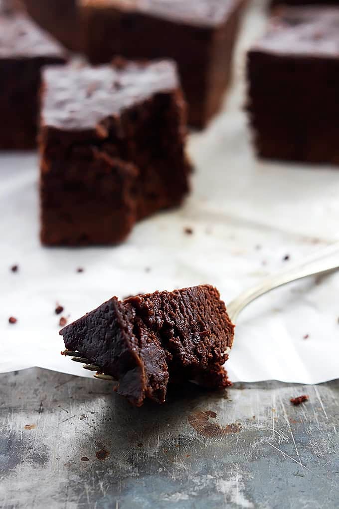 a fork with a slow cooker brownies bite on it with brownies in the background with the front one missing a bite.