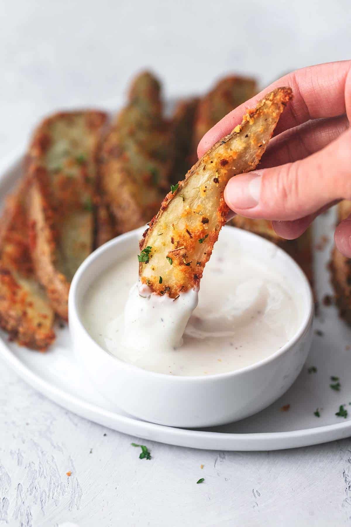 hand dipping potato wedge in ranch