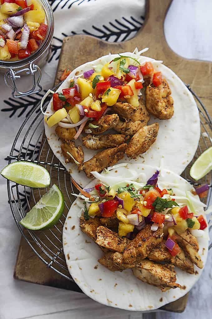 Caribbean chicken tacos and slices of limes on a round cooling rack on a wooden cutting board.