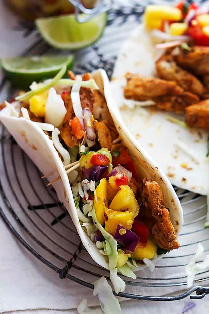 Caribbean chicken tacos on a round cooling rack with lime slices on the side.