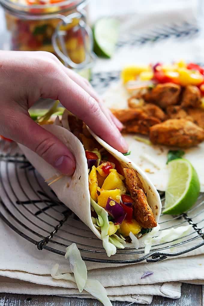 a hand holding a Caribbean chicken taco with another taco on the side.