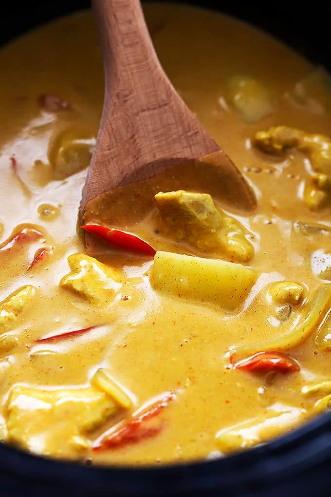 close up of slow cooker coconut curry cashew chicken and a wooden serving spoon.