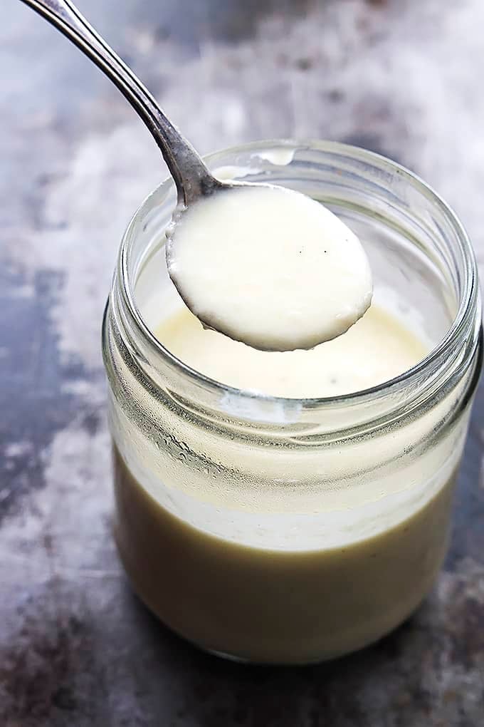a spoon with Greek yogurt alfredo sauce on it being lifted from a jar of sauce.