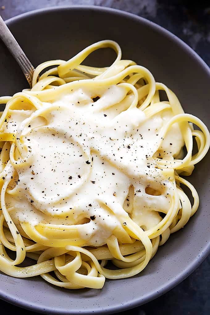 top view of fettucine noodles with Greek yogurt alfredo sauce on top and a fork in a bowl.