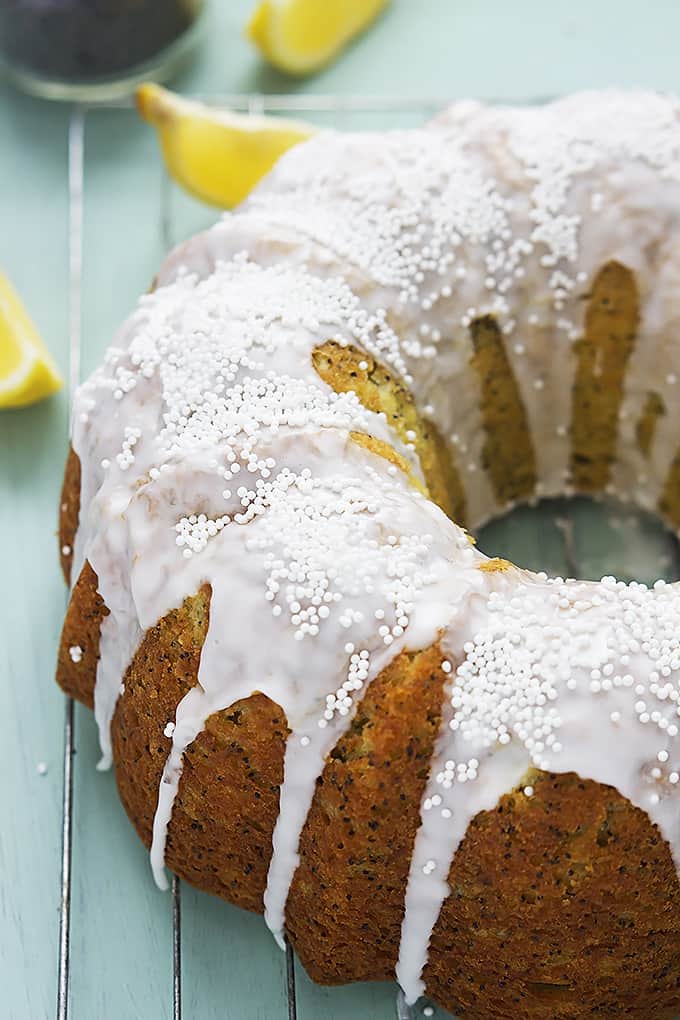 lemon poppyseed bundt cake on a cooling rack with slices of lemon in the background.