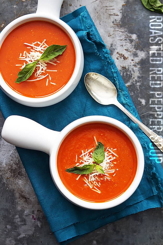 top view of two bowls of roasted red pepper soup with a spoon on the side and the title of the recipe written vertically on the right side of the image.