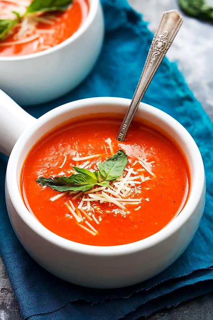 roasted red pepper soup and a spoon in a bowl with another bowl of soup on the background.