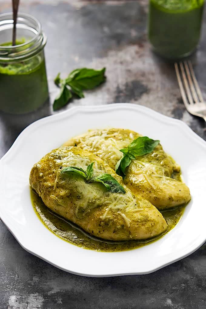 slow cooker pesto ranch chicken on a plate with a fork and jars of pesto in the background.