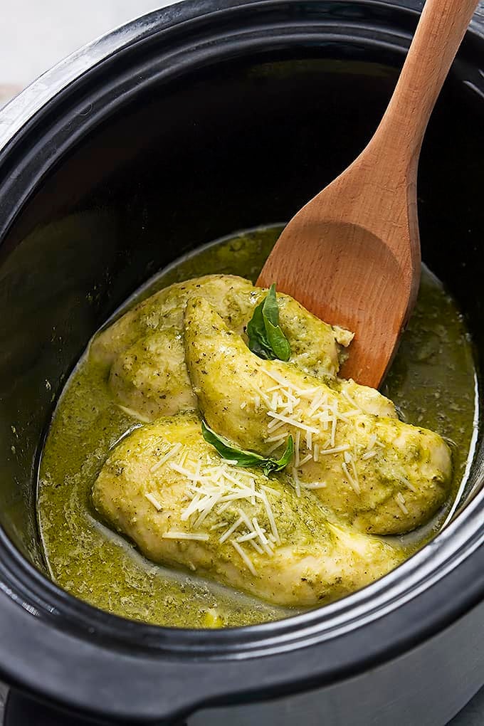 slow cooker pesto ranch chicken and a wooden serving spoon in a slow cooker.