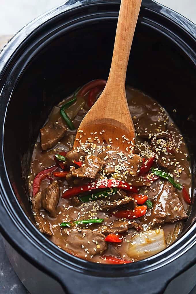 top view of slow cooker sesame beef with a wooden spoon in a slow cooker.