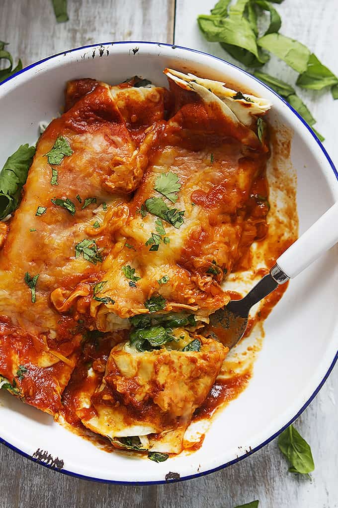 top view of cheesy spinach enchiladas with a bite on a fork in a bowl.