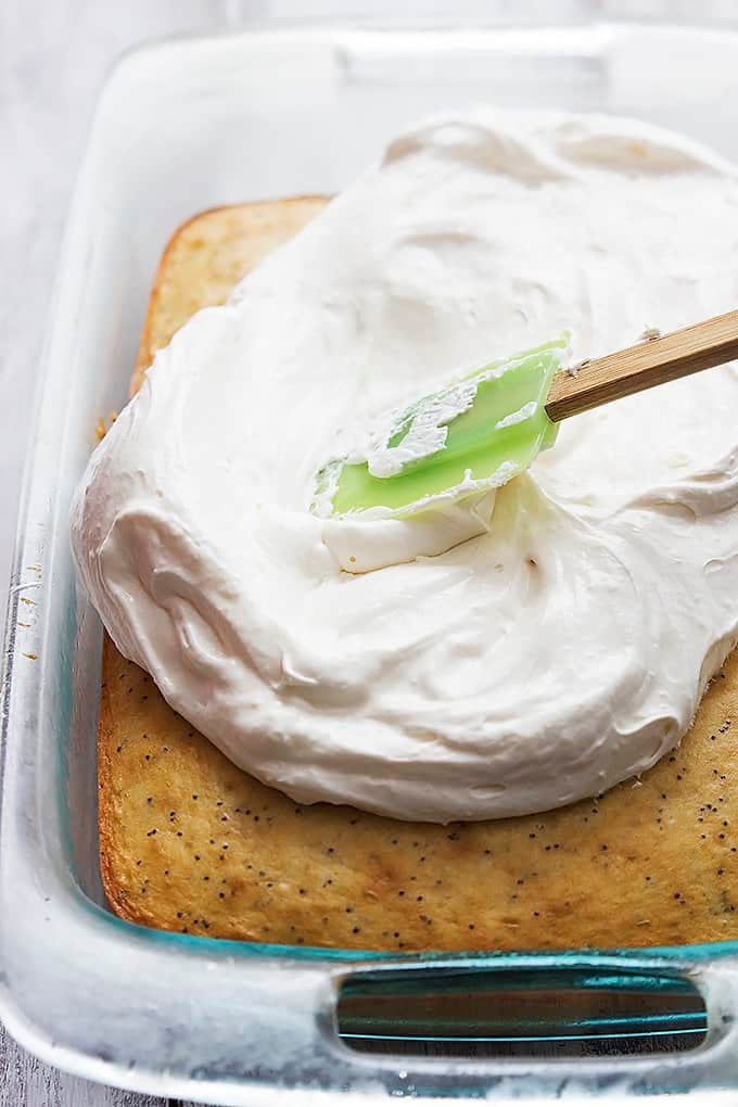 a spatula frosting strawberry poppyseed cake in a glass cooking pan.