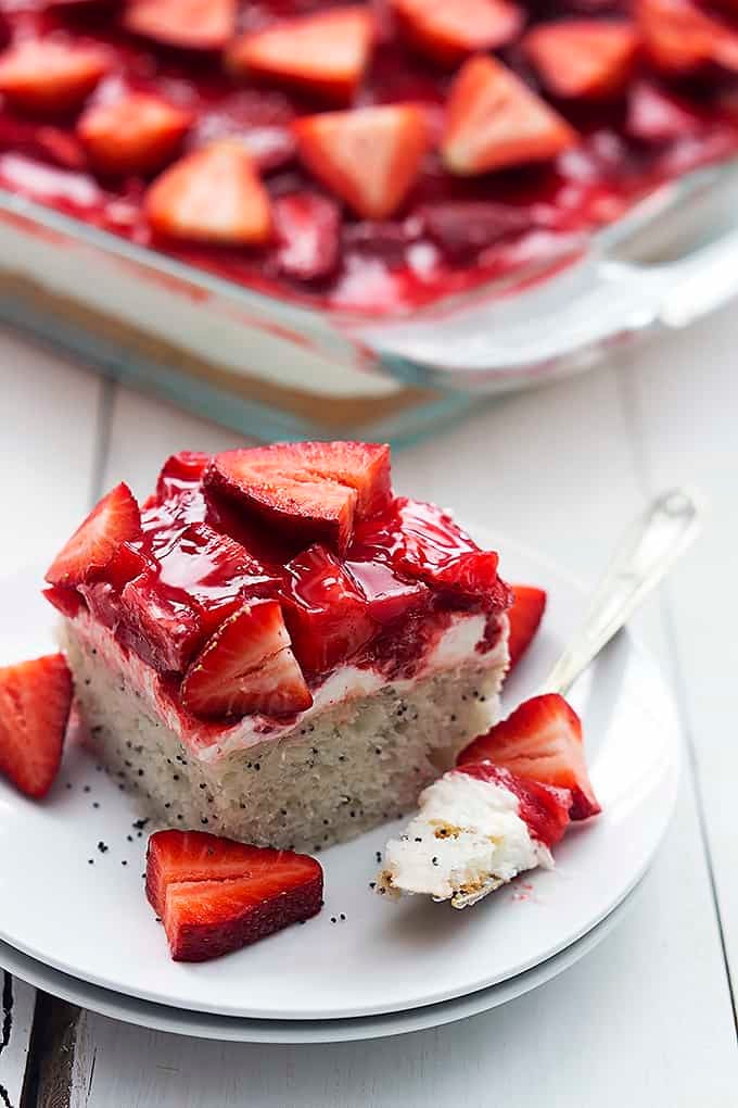 a piece of strawberry poppyseed cake and a fork with a bite on it on a plate with more cake in a glass cake pan.
