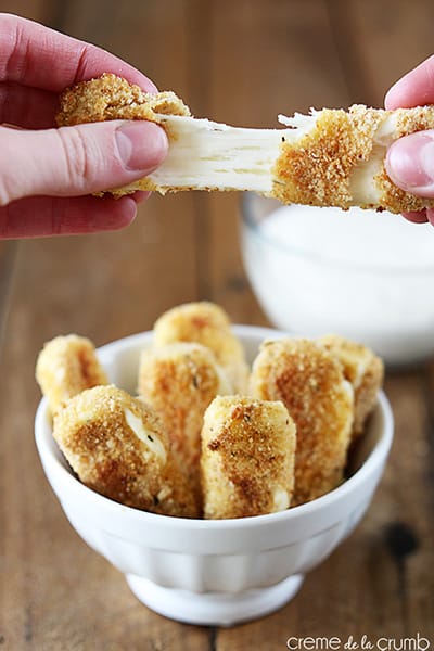 hands pulling apart of baked mozzarella stick above a bowl of mozzarella sticks.