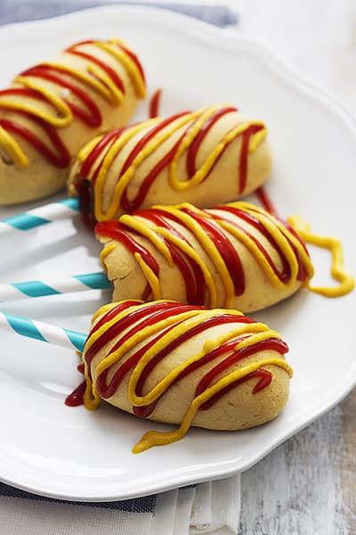 baked Bisquick corn dogs on a stick and topped with mustard and ketchup on a plate.