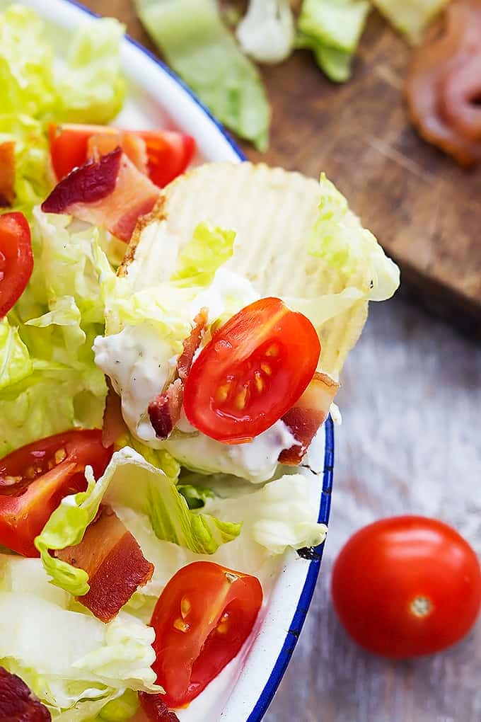 close up of creamy Ranch BLT dip in a bowl with a chip dipped inside.