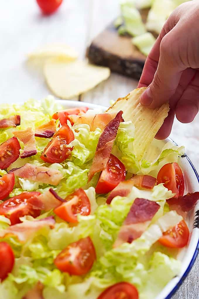 a hand dipping a chip in a bowl of creamy Ranch BLT dip.