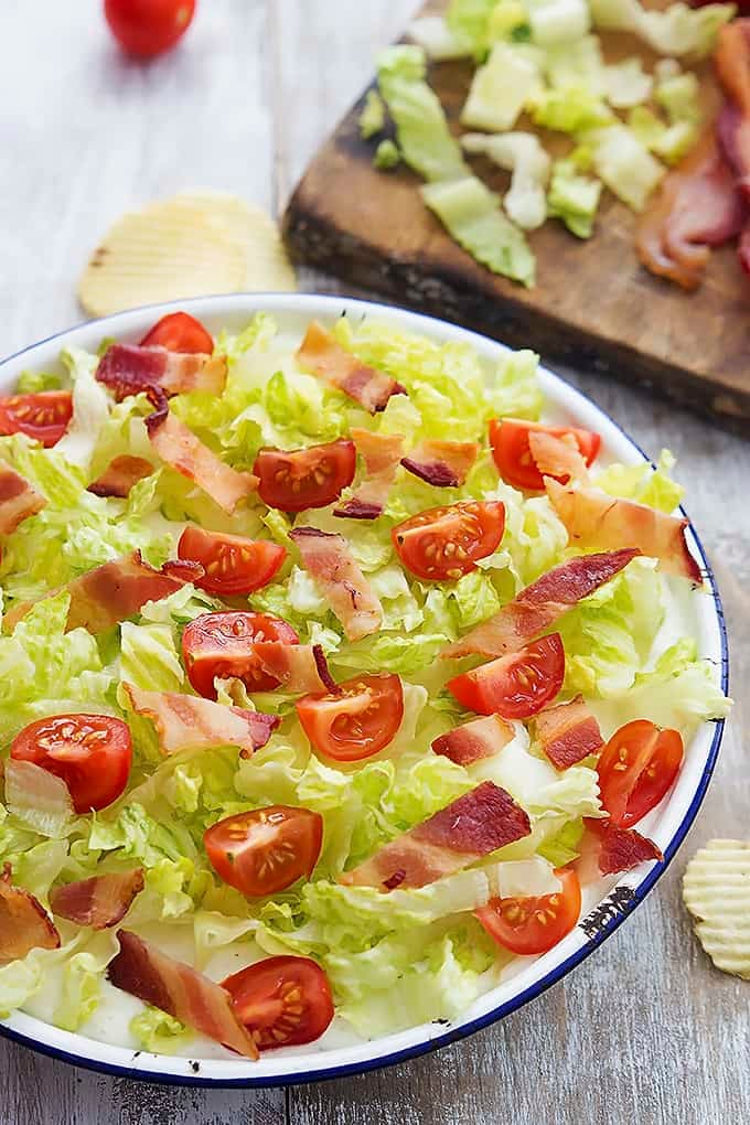 creamy Ranch BLT dip in a bowl with chips and toppings on the side and on a wooden cutting board.