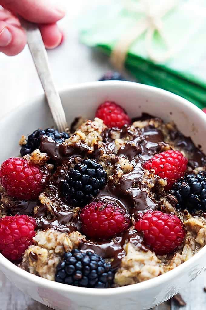 close up of a hand holding a spoon inside a bowl of choco-berry oatmeal.