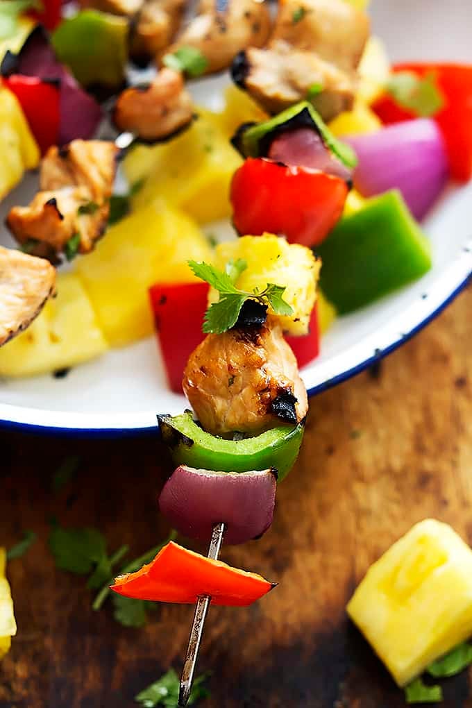 close up of a grilled Hawaiian chicken kabob laying across a bowl next to more kabobs.