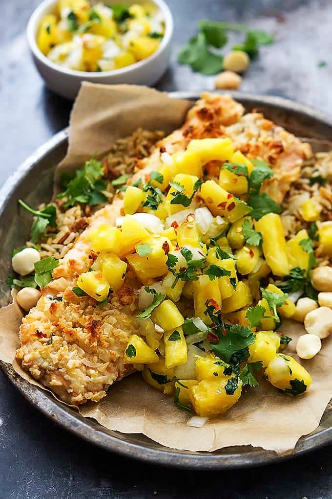 macadamia salmon with pineapple salsa on a round metal plate with a small bowl of salsa in the background.