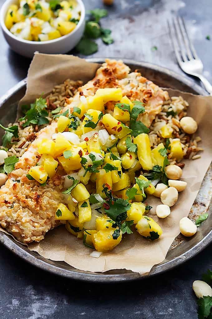 macadamia salmon with pineapple salsa on a round metal plate with a fork and a small bowl of salsa on the side.