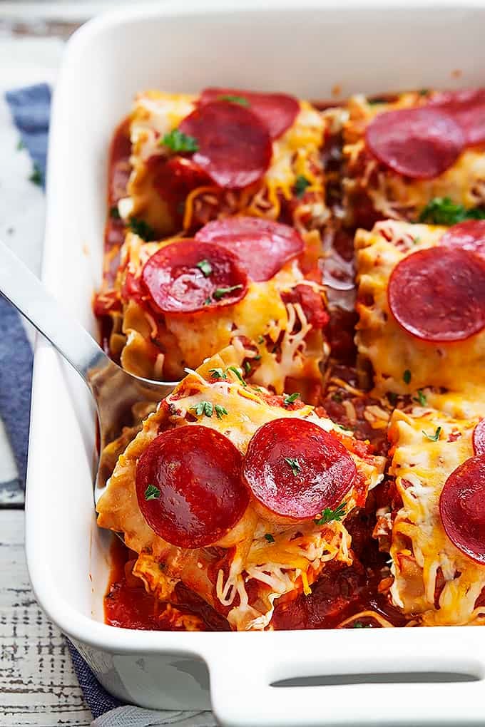 a spatula picking up a pepperoni pizza lasagna roll up from a baking sheet full of warm ups.