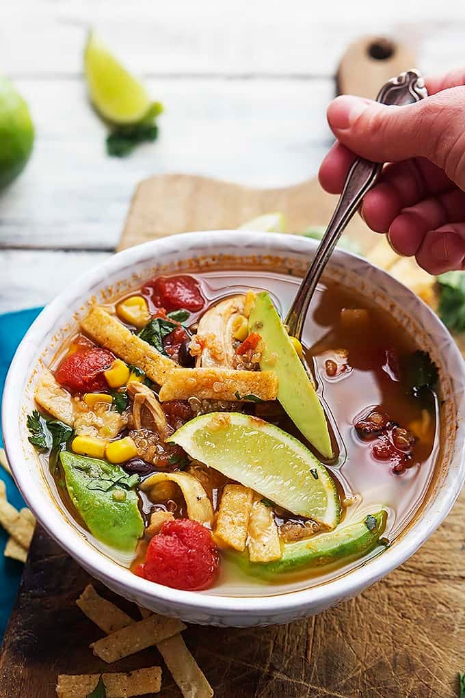 a hand holding a spoon in a bowl of quinoa chicken tortilla soup.