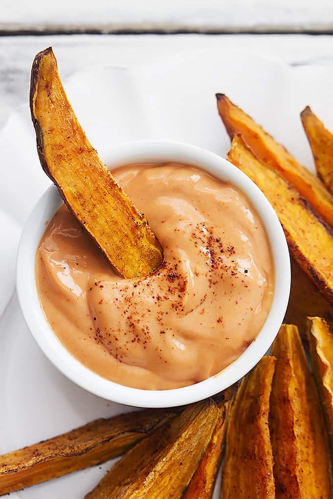 top view of a spicy baked sweet potato wedge dipped in a small bowl of fry sauce with more potato wedges on the side.